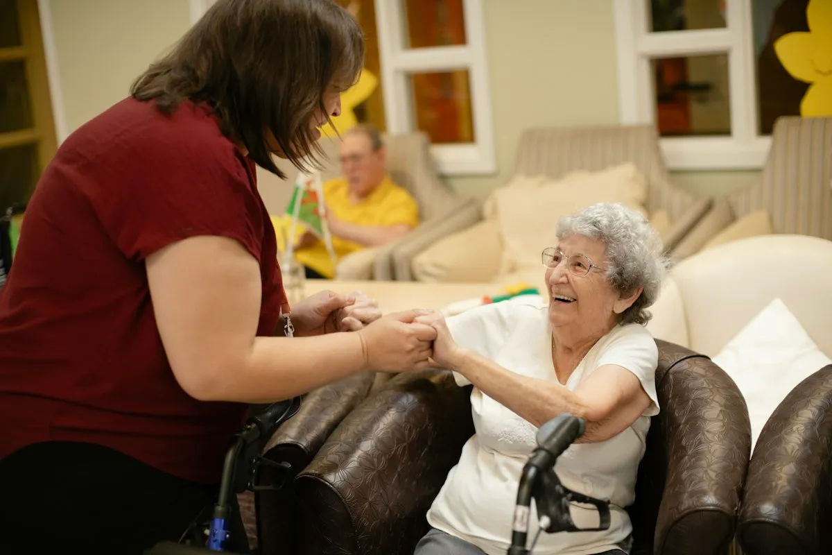 Pflegekraft hilft einer Seniorin mit Rollator beim Aufstehen